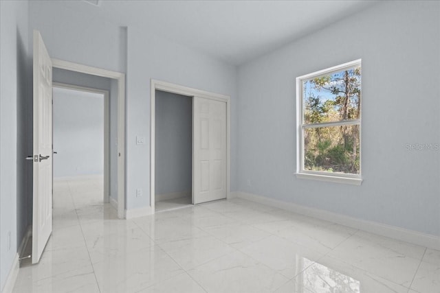 unfurnished bedroom featuring marble finish floor, a closet, and baseboards