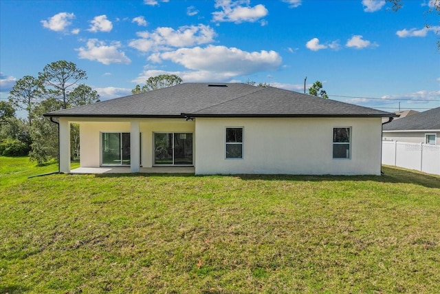 rear view of house with stucco siding, fence, a lawn, and a patio