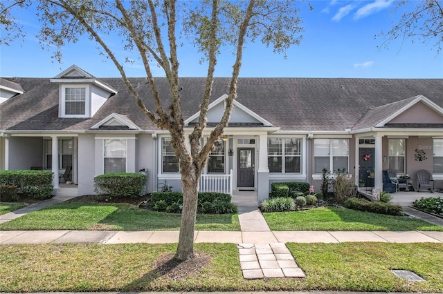 townhome / multi-family property featuring covered porch, roof with shingles, a front lawn, and stucco siding