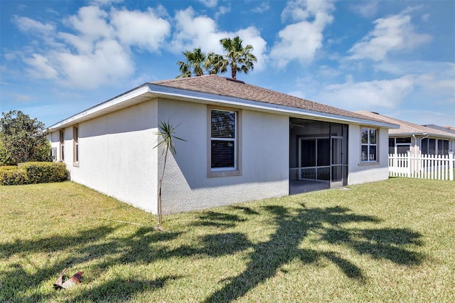 rear view of property featuring stucco siding, a sunroom, a yard, and fence