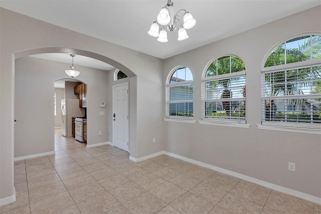 empty room featuring a notable chandelier, baseboards, arched walkways, and light tile patterned floors