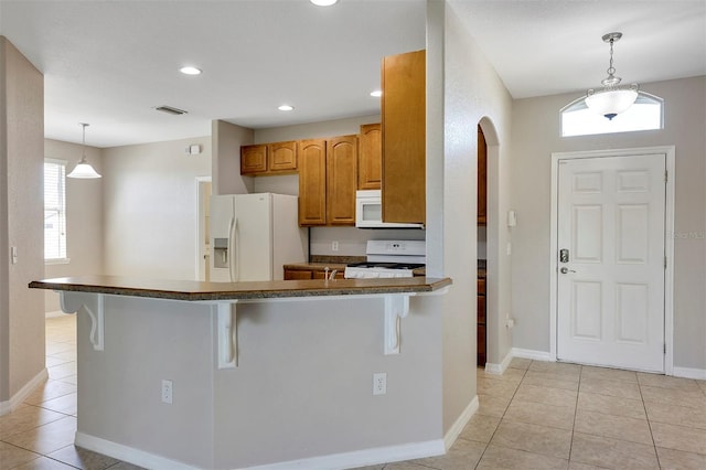 kitchen featuring dark countertops, a breakfast bar area, light tile patterned floors, arched walkways, and white appliances