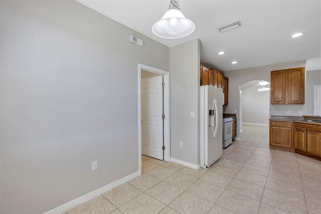 kitchen featuring visible vents, baseboards, brown cabinets, arched walkways, and white appliances