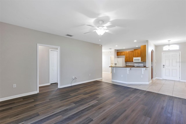 unfurnished living room featuring visible vents, ceiling fan with notable chandelier, baseboards, and wood finished floors