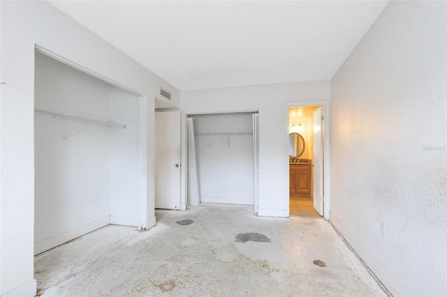 unfurnished bedroom with visible vents, two closets, ensuite bathroom, baseboards, and concrete flooring