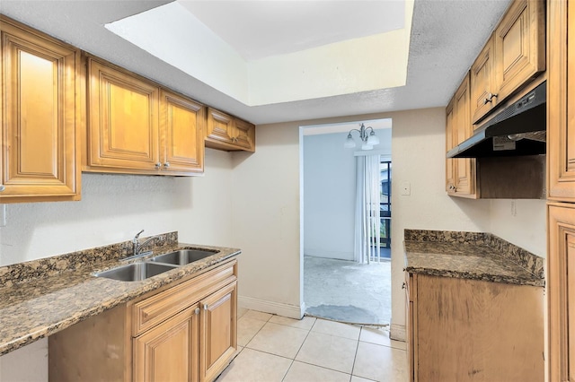 kitchen with dark stone countertops, light tile patterned floors, baseboards, a sink, and under cabinet range hood