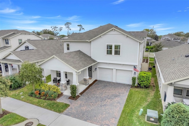 view of front of property with a residential view, roof with shingles, covered porch, decorative driveway, and a front lawn