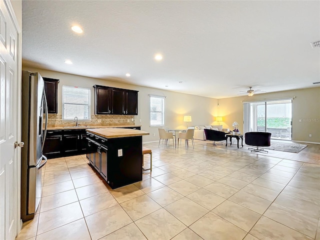 kitchen with decorative backsplash, open floor plan, a center island, stainless steel refrigerator with ice dispenser, and light tile patterned flooring