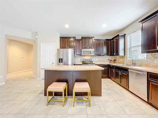 kitchen featuring a kitchen island, a kitchen breakfast bar, stainless steel appliances, light countertops, and a sink