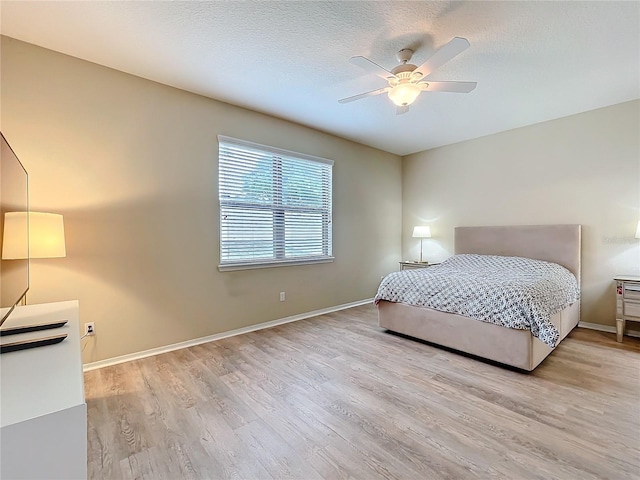 bedroom with light wood-type flooring, ceiling fan, baseboards, and a textured ceiling