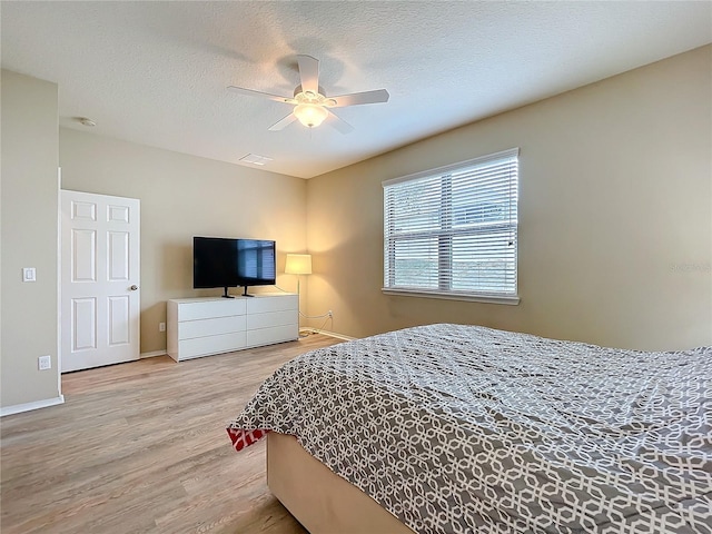 bedroom with a ceiling fan, light wood-style flooring, visible vents, and a textured ceiling