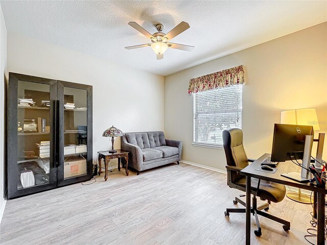 office featuring light wood-type flooring, baseboards, a ceiling fan, and a textured ceiling