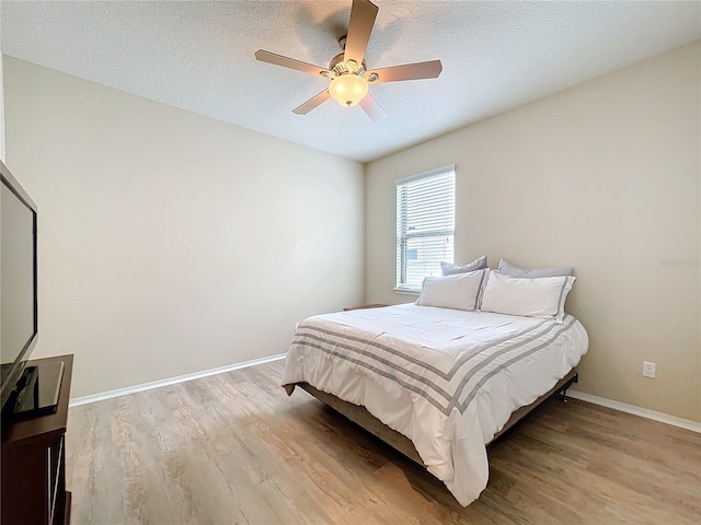 bedroom with light wood-type flooring, ceiling fan, a textured ceiling, and baseboards