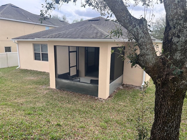 rear view of property featuring roof with shingles, a lawn, fence, and stucco siding