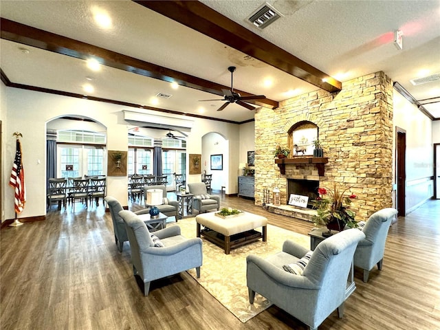 living area with arched walkways, a stone fireplace, wood finished floors, visible vents, and beam ceiling