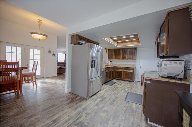 kitchen featuring decorative backsplash, light stone counters, appliances with stainless steel finishes, a tray ceiling, and light wood-style floors