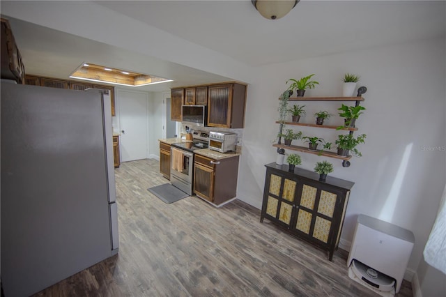 kitchen with a raised ceiling, stainless steel appliances, wood finished floors, and light countertops