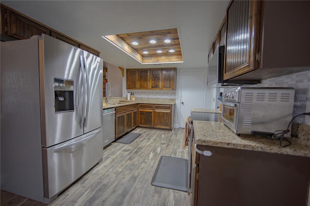 kitchen featuring a tray ceiling, decorative backsplash, appliances with stainless steel finishes, a sink, and light wood-type flooring