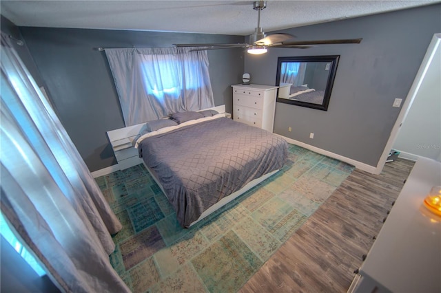 bedroom with a ceiling fan, a textured ceiling, baseboards, and wood finished floors