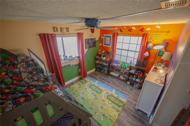 bedroom with a textured ceiling, wood finished floors, visible vents, and baseboards