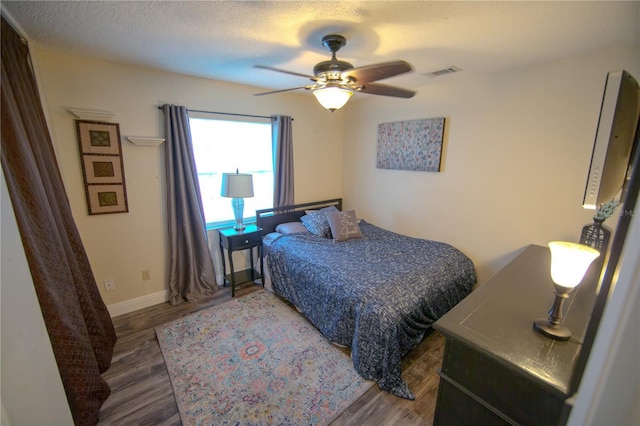 bedroom with a textured ceiling, wood finished floors, a ceiling fan, visible vents, and baseboards