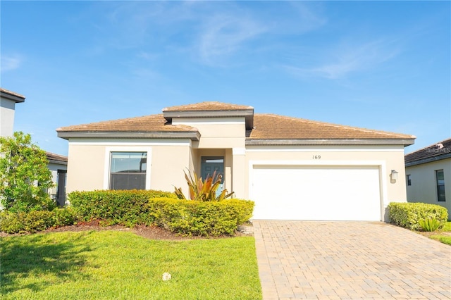 prairie-style house featuring an attached garage, stucco siding, decorative driveway, and a front yard