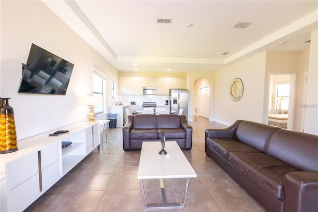 tiled living area featuring arched walkways, recessed lighting, a raised ceiling, visible vents, and baseboards