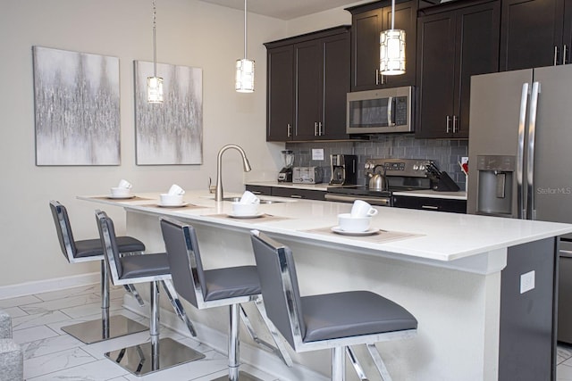 kitchen featuring an island with sink, appliances with stainless steel finishes, a kitchen breakfast bar, hanging light fixtures, and light countertops