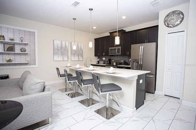 kitchen with marble finish floor, hanging light fixtures, appliances with stainless steel finishes, and a center island with sink