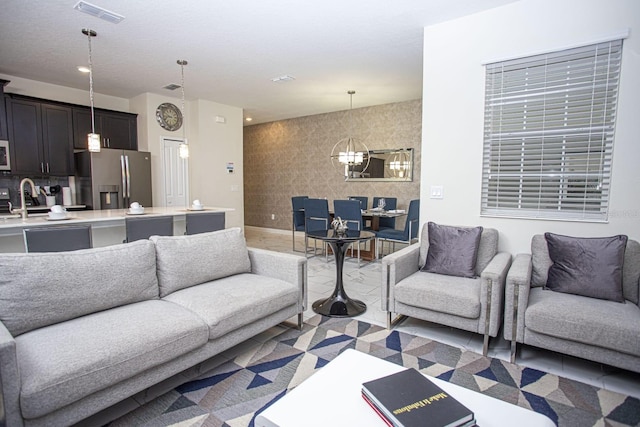 living room with baseboards, an accent wall, visible vents, and a notable chandelier