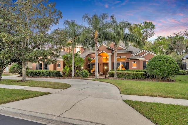 view of front of house featuring driveway, a lawn, and stucco siding