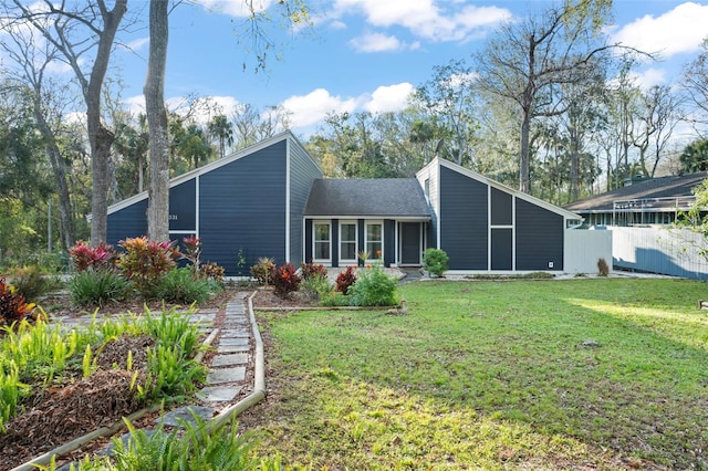 rear view of house with a shingled roof, fence, and a lawn