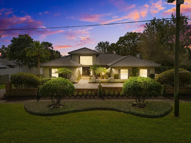 mediterranean / spanish home featuring a tile roof, a lawn, fence, and stucco siding