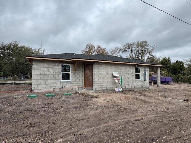 view of front facade with a shingled roof and concrete block siding