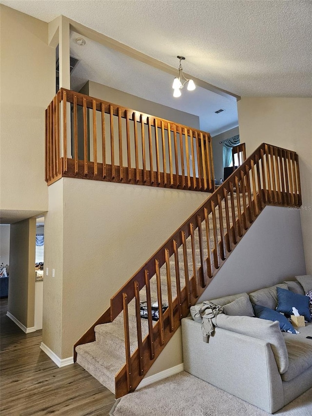 stairs featuring a chandelier, a textured ceiling, baseboards, and wood finished floors