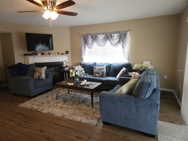 living area with a textured ceiling, a fireplace, wood finished floors, a ceiling fan, and baseboards