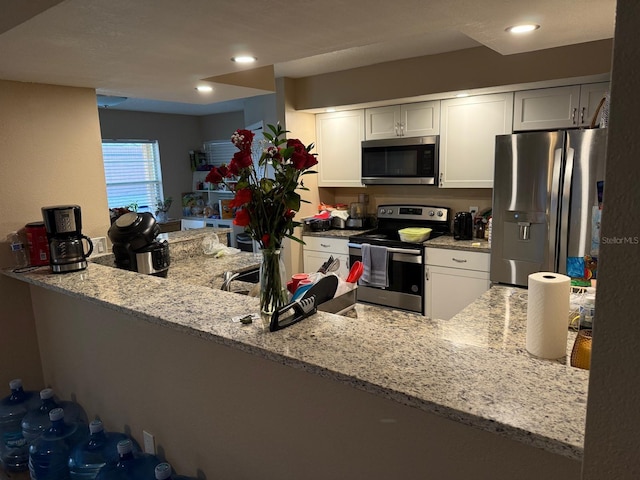 kitchen with light stone counters, recessed lighting, a peninsula, white cabinets, and appliances with stainless steel finishes