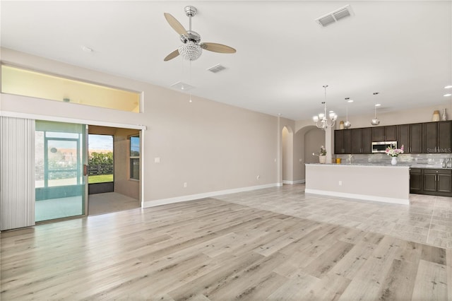 unfurnished living room with light wood-style flooring, visible vents, arched walkways, and ceiling fan with notable chandelier