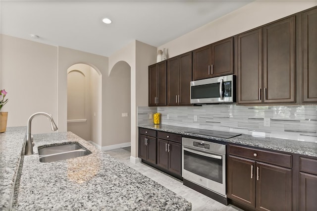 kitchen featuring tasteful backsplash, light stone counters, stainless steel appliances, and a sink