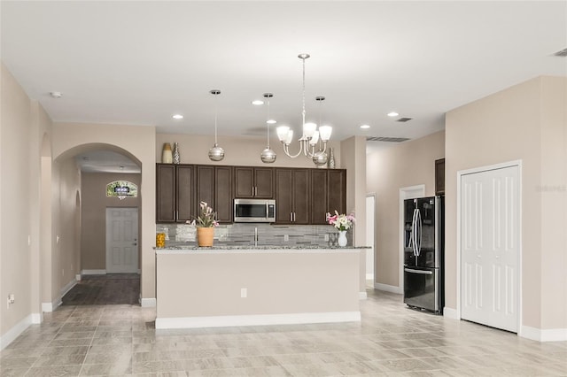 kitchen with arched walkways, dark brown cabinetry, black fridge, backsplash, and stainless steel microwave