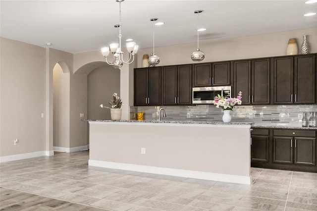 kitchen featuring arched walkways, stainless steel microwave, a sink, and decorative backsplash