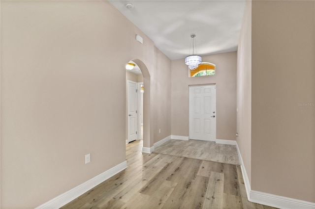 foyer entrance featuring light wood-style floors, baseboards, arched walkways, and an inviting chandelier