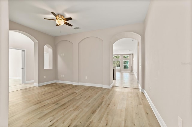 empty room featuring baseboards, visible vents, arched walkways, a ceiling fan, and light wood-type flooring