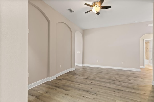 spare room with arched walkways, a ceiling fan, baseboards, visible vents, and light wood-style floors