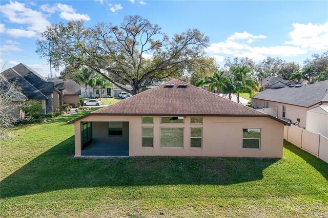 back of house featuring roof with shingles, a lawn, fence, and stucco siding