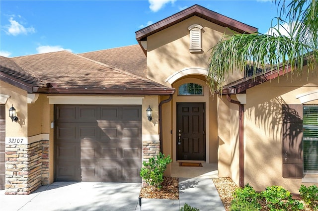 entrance to property with a shingled roof, an attached garage, and stucco siding