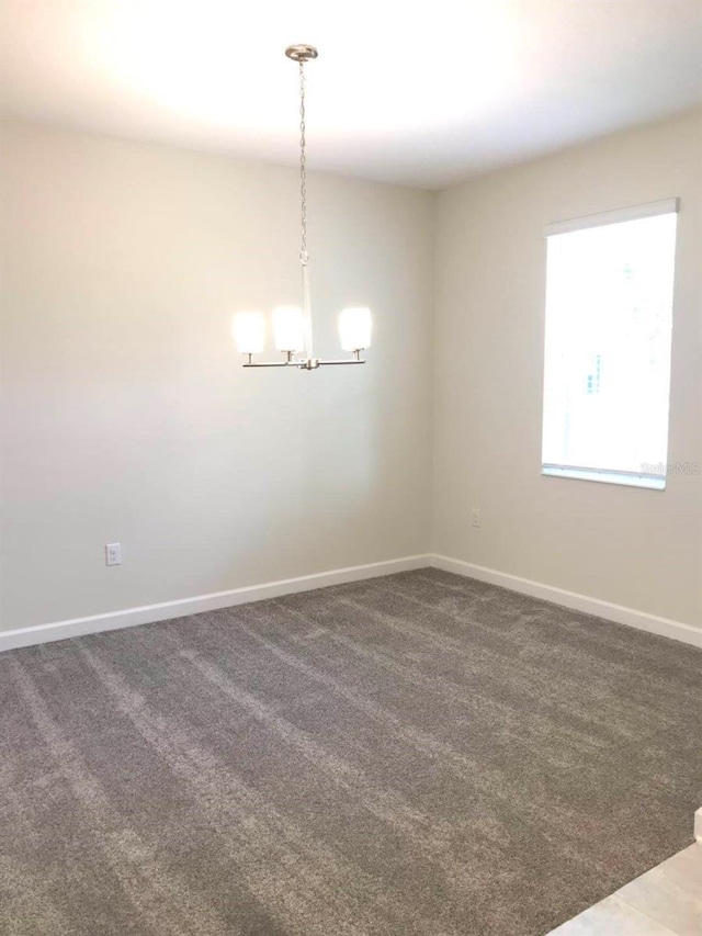 empty room featuring carpet flooring, a notable chandelier, and baseboards