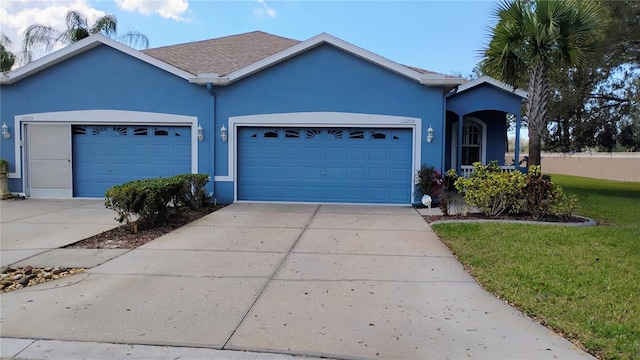 ranch-style home featuring driveway, roof with shingles, an attached garage, a front lawn, and stucco siding