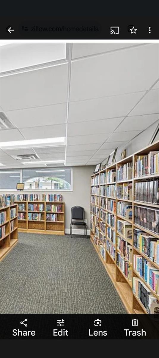 12209 Putter Green Ct, New Port Richey, FL 34654 - living area with wall of books, a paneled ceiling, and carpet flooring
