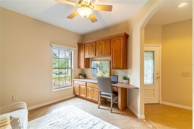 home office with arched walkways, light tile patterned floors, a ceiling fan, built in study area, and baseboards